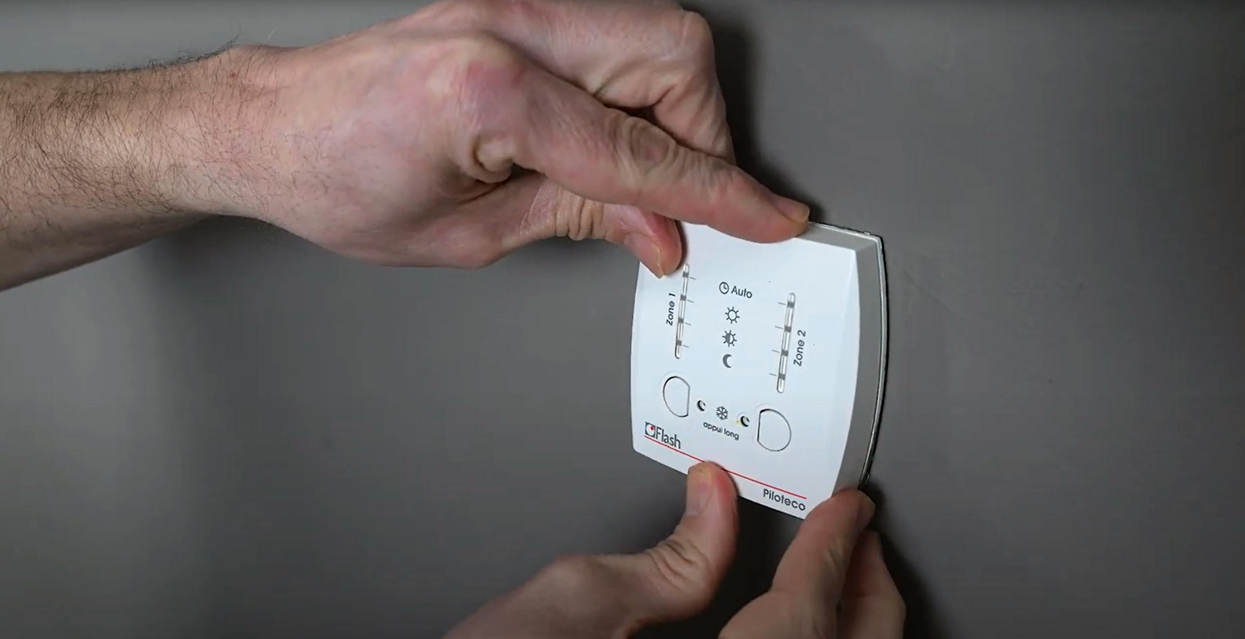 Deux mains fixant un thermostat programmable blanc sur un mur