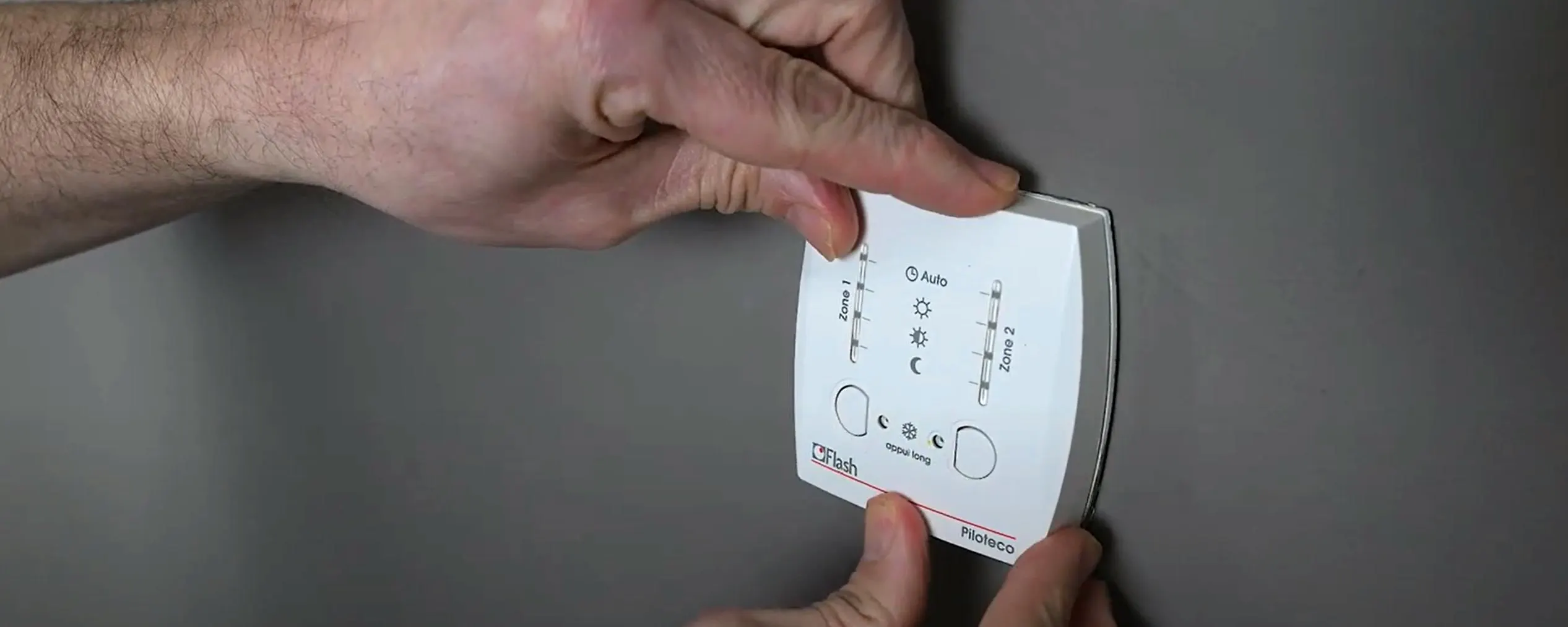 Deux mains en train de changer un thermostat d'ambiance programmable blanc sur un mur