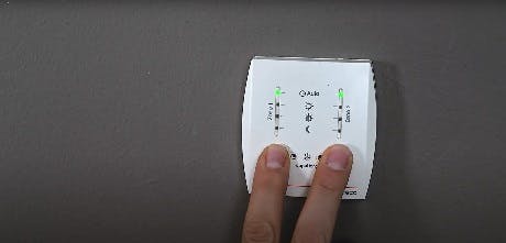 Deux doigts appuyant sur les boutons d'un thermostat mural blanc