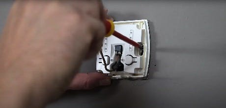 Main branchant un fil électrique sur un thermostat mural