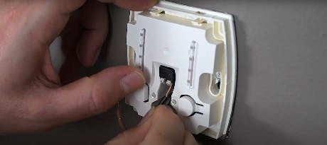 Main connectant des fils électriques à l'arrière d'un thermostat