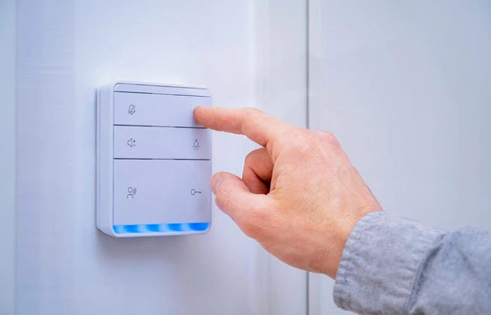 Main appuyant sur un interrupteur domotique blanc avec LED bleues