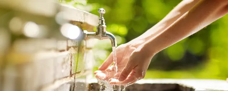 Mains se rinçant sous un robinet extérieur en pierre fraîchement installé au soleil