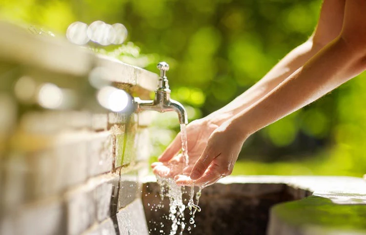 Mains se rinçant sous un robinet extérieur en pierre au soleil