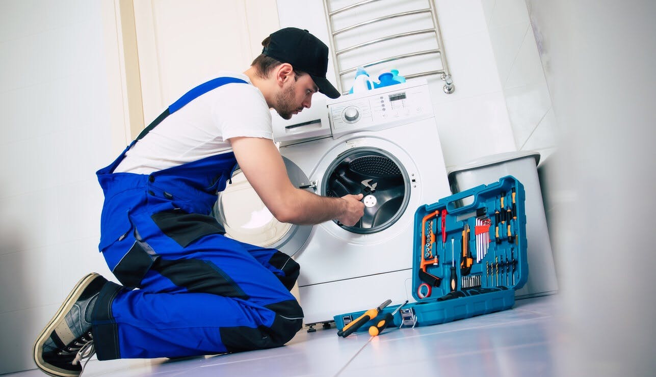 Technicien en bleu de travail réparant une machine à laver avec ses outils