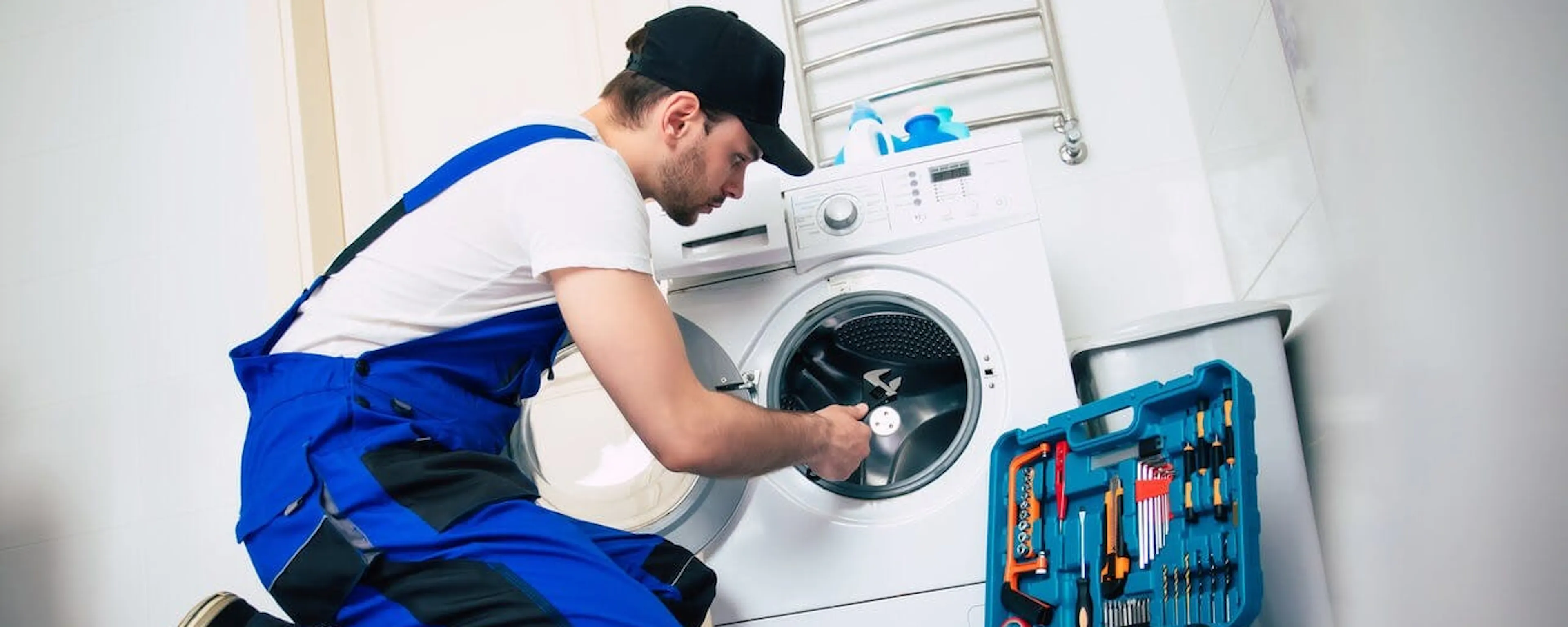 Technicien en bleu réparant une machine à laver avec des outils