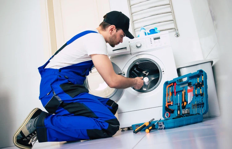 Technicien en bleu de travail réparant une machine à laver avec ses outils