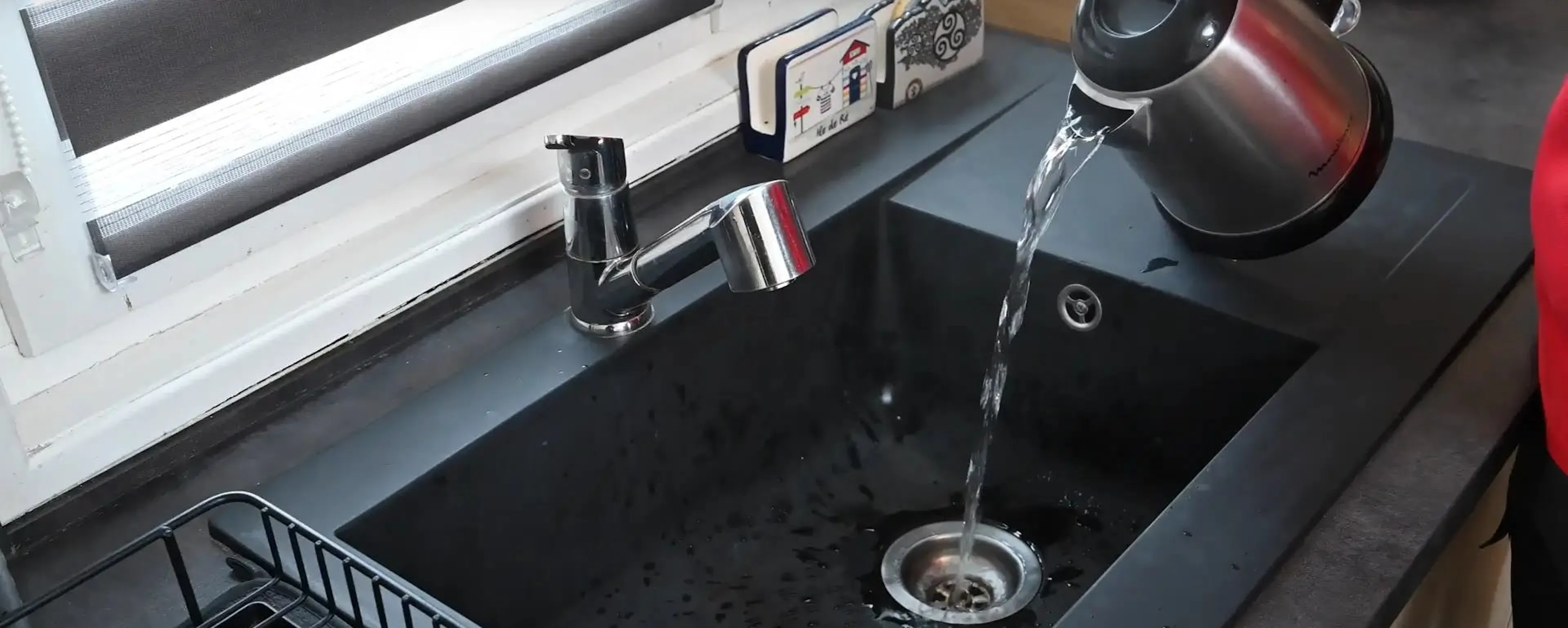 Évier noir avec bouilloire versant de l'eau afin de nettoyer les canalisations avec des produits naturels