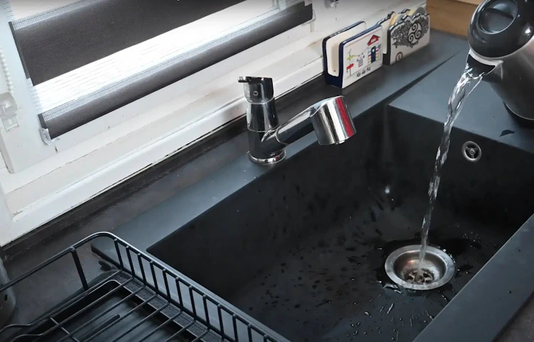 Évier de cuisine noir avec bouilloire versant de l'eau
