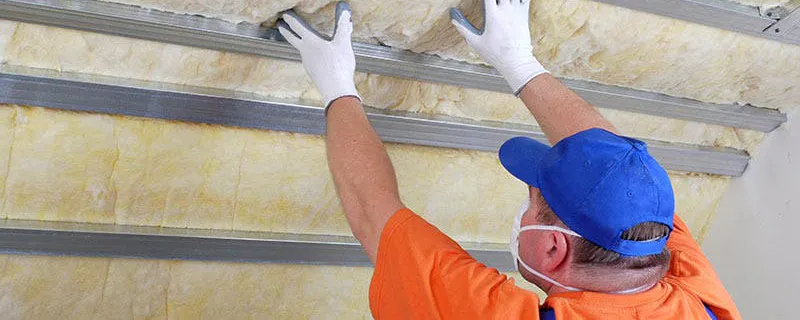 Ouvrier posant des rouleaux de laine de verre pour isoler un faux plafond