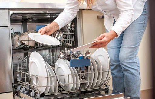 Femme chargeant des assiettes et couverts dans un lave-vaisselle ouvert