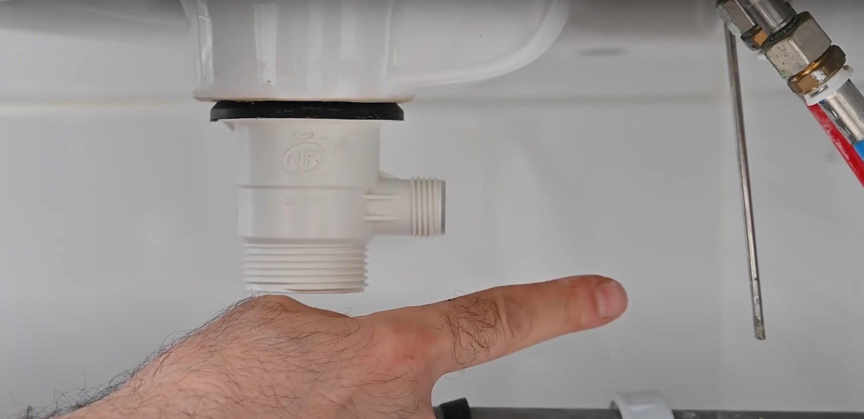 Main montrant le siphon plastique blanc sous un évier