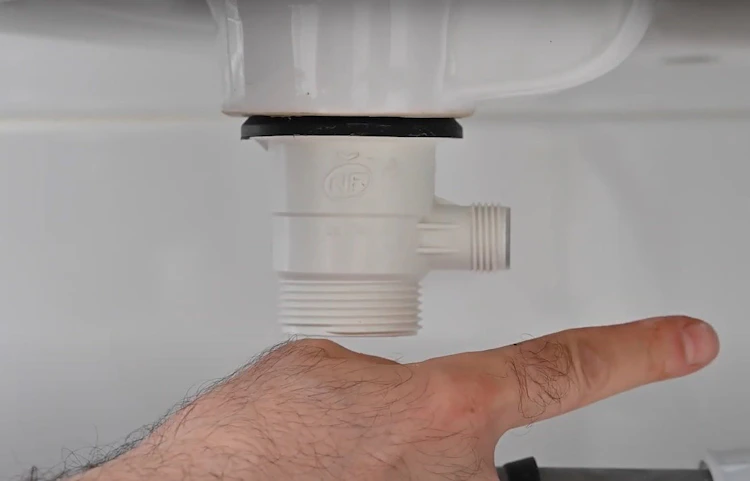 Main montrant le siphon plastique blanc sous un évier