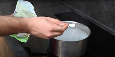 Main plaçant un pastille dans une casserole d'eau bouillante