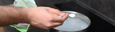 Main plaçant un pastille dans une casserole d'eau bouillante