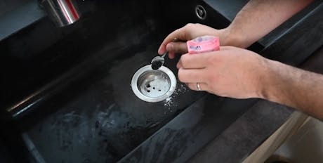 Mains saupoudrant du produit dans la bonde d'un évier noir