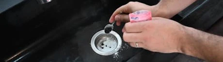 Mains saupoudrant du produit dans la bonde d'un évier noir