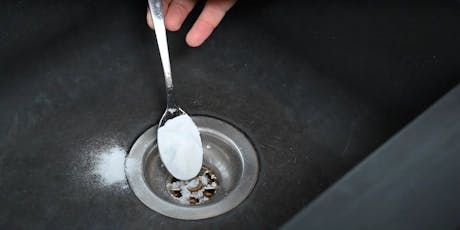 Cuillère versant de la poudre blanche dans la bonde d'un évier