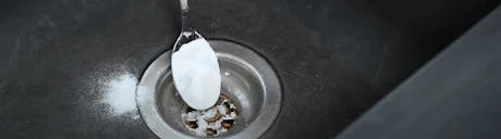 Cuillère versant de la poudre blanche dans la bonde d'un évier