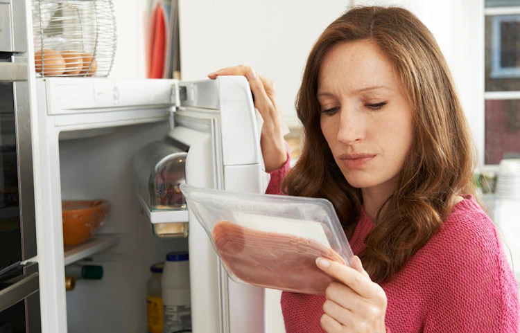 Femme inquiète inspectant un aliment devant un réfrigérateur ouvert