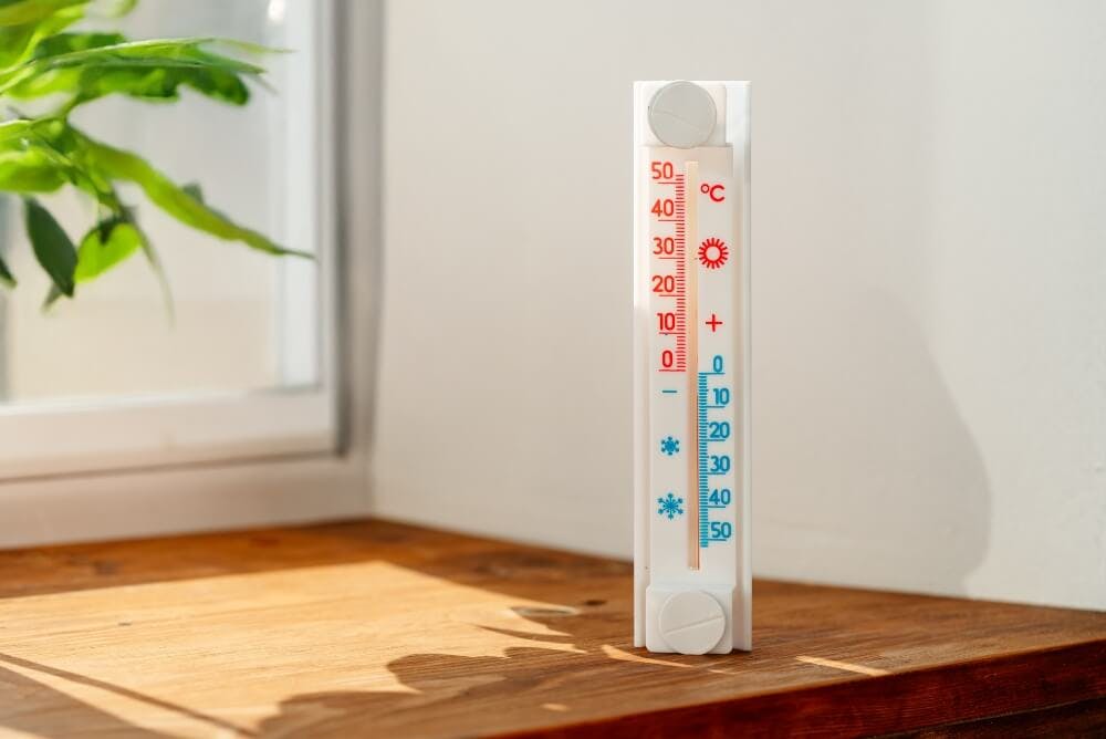 Thermomètre mural posé sur un rebord en bois près d'une fenêtre