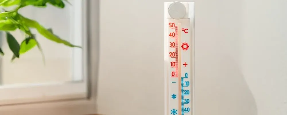 Thermomètre mural sur un rebord en bois près d'une fenêtre aidant à optimiser la capacité de chauffage