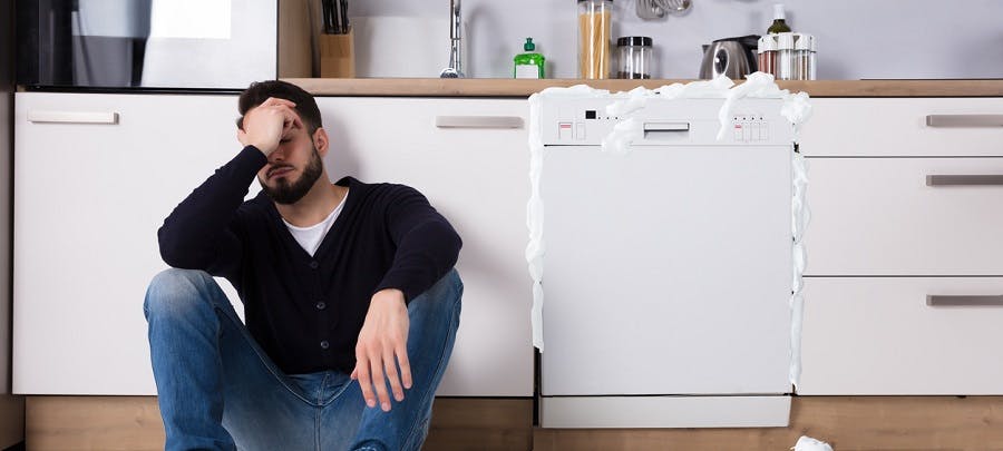 Homme assis par terre dans sa cuisine devant un lave-vaisselle ouvert