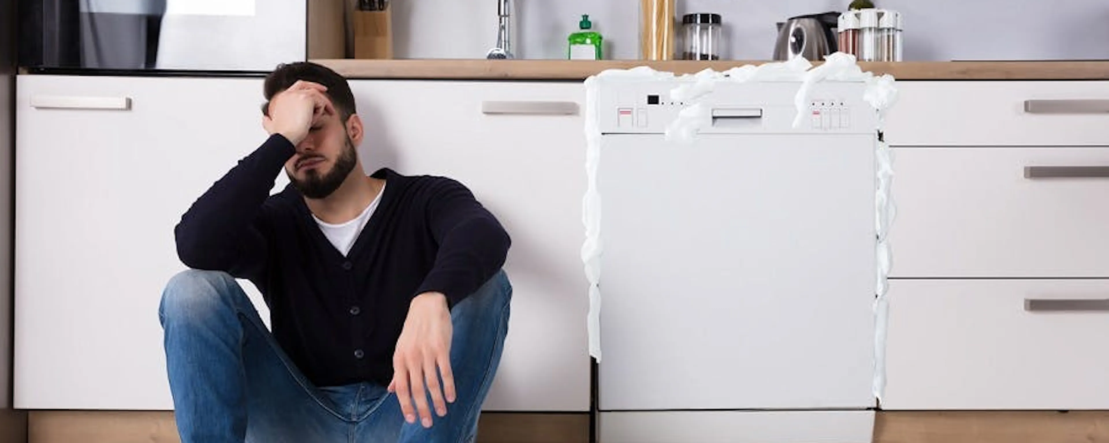 Homme assis devant un lave-vaisselle en panne dans sa cuisine se demandant si la panne allait être prise en charge par l'assurance habitation