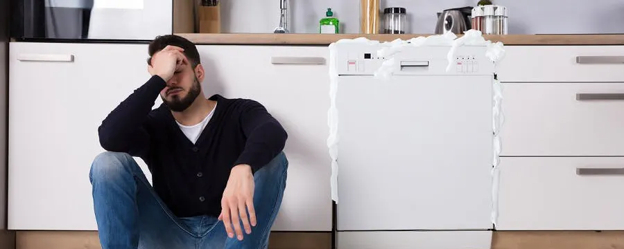 Homme assis devant un lave-vaisselle en panne dans sa cuisine se demandant si la panne allait être prise en charge par l'assurance habitation