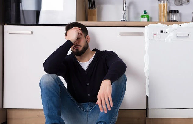 Homme assis par terre dans sa cuisine devant un lave-vaisselle ouvert