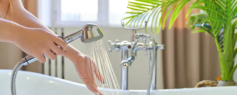 Femme testant le faible débit d'une douchette car elle n'a plus de pression d'eau chaude