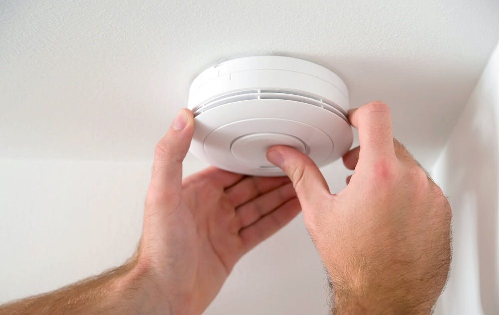 Personne installant un détecteur de fumée blanc au plafond à deux mains