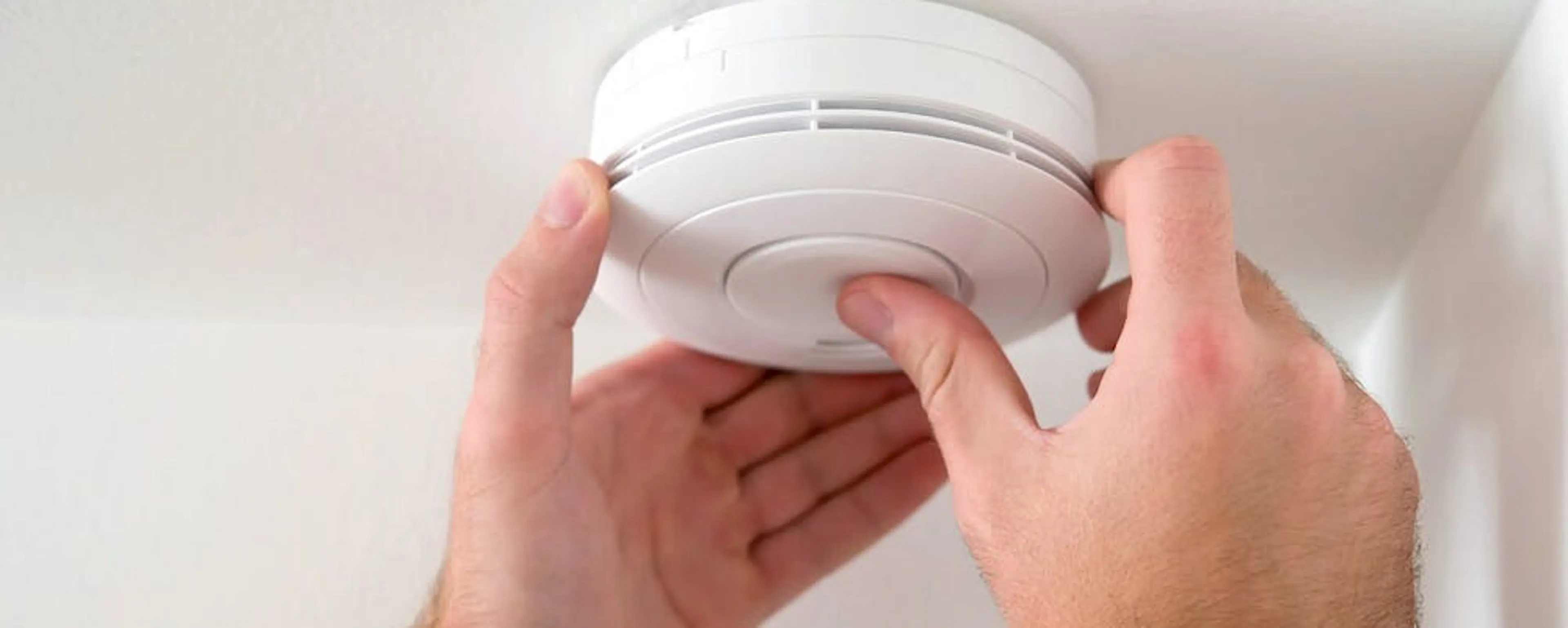 Doigt appuyant sur le bouton d'arrêt d'un détecteur de fumée qui sonne