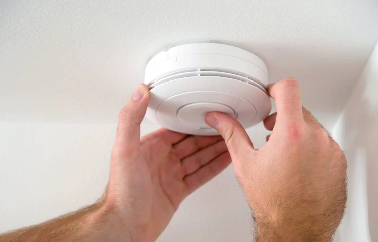 Personne installant un détecteur de fumée blanc au plafond à deux mains