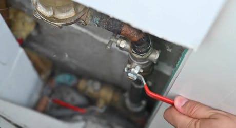 Main fermant une vanne d'arrivée d'eau avec une pince