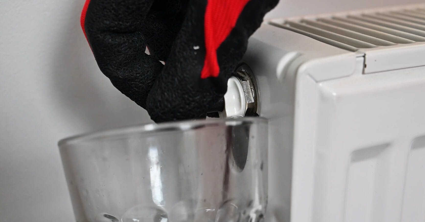 Main gantée purgeant un radiateur blanc au-dessus d'un récipient