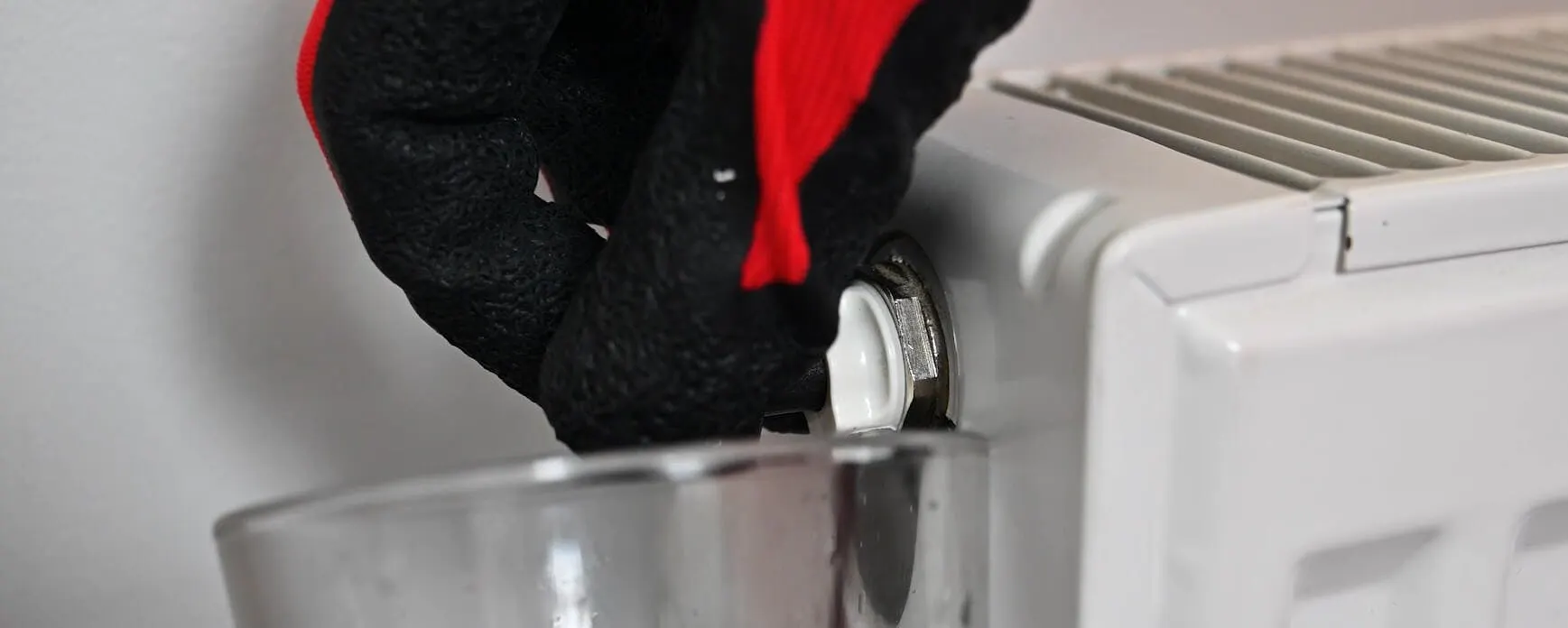 Main gantée purgeant un radiateur blanc encrassé au-dessus d'un récipient