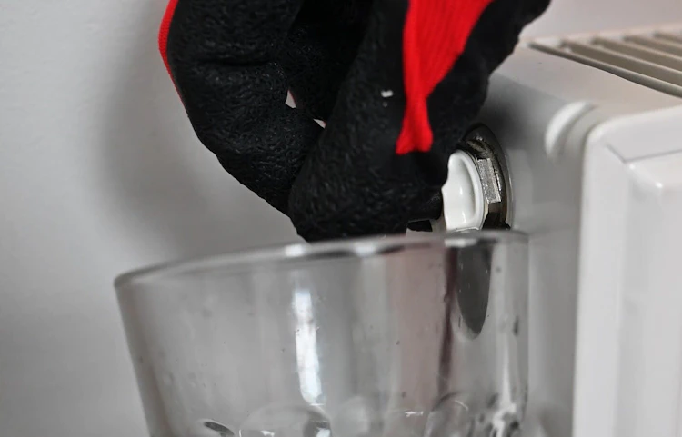 Main gantée purgeant un radiateur blanc au-dessus d'un récipient