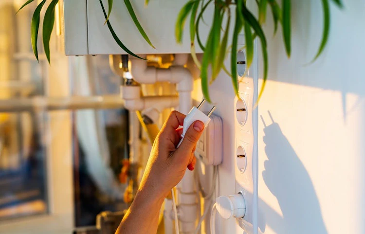 Main branchant une fiche électrique dans une prise murale blanche