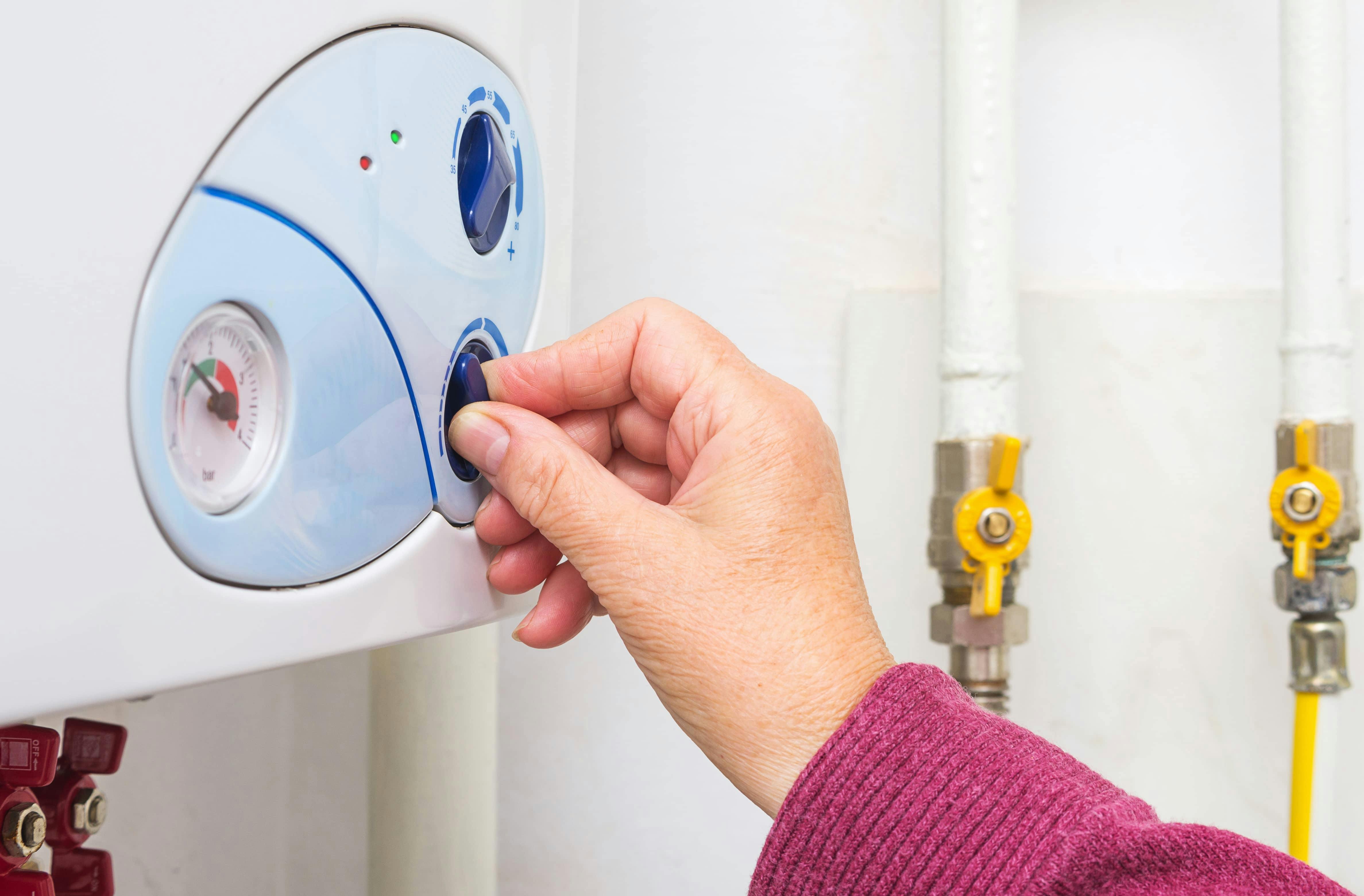Main réglant le thermostat d'un chauffe-eau mural blanc