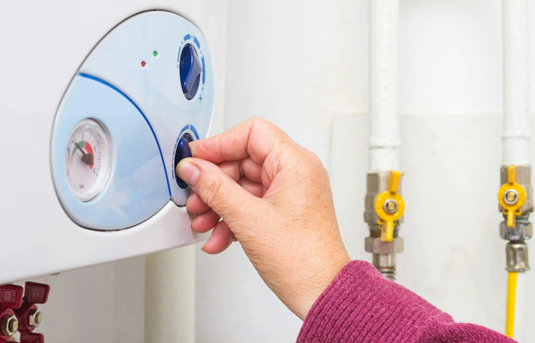 Main réglant le thermostat d'un chauffe-eau mural blanc