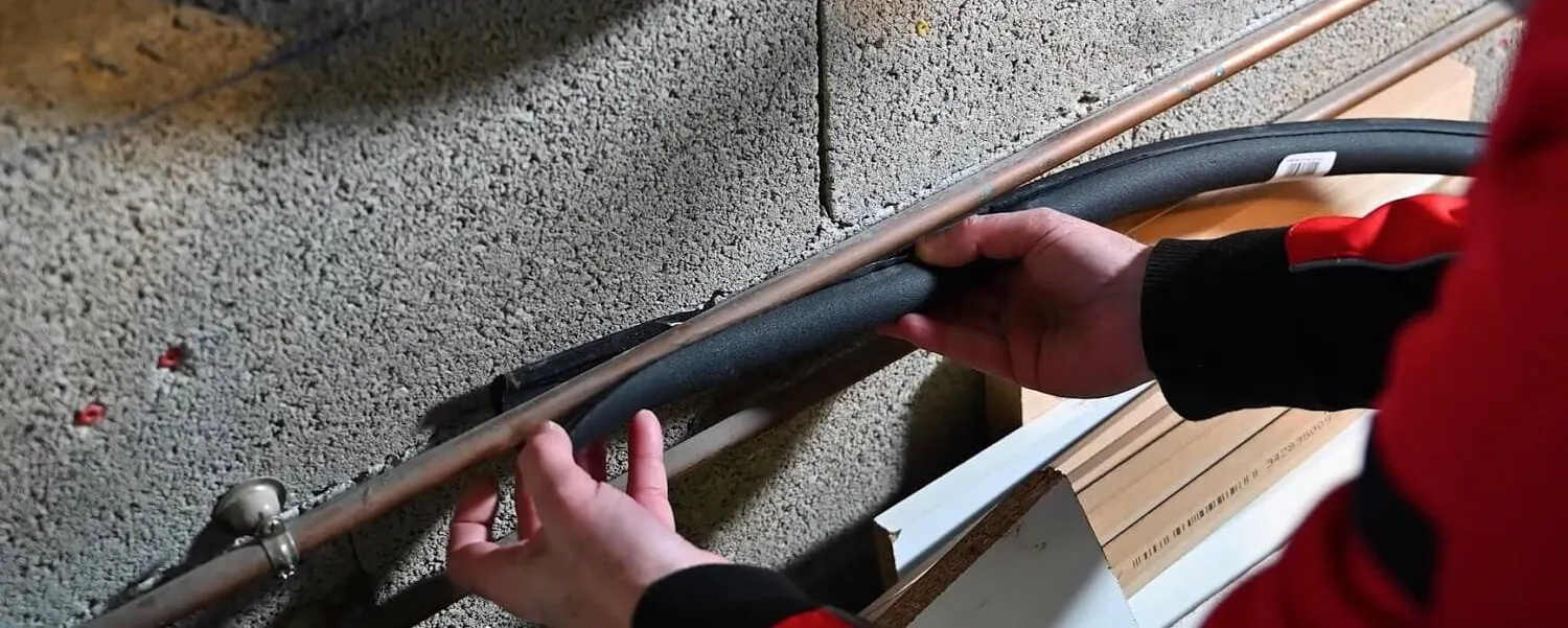 Mains posant un câble le long d'un mur en béton pour protéger les canalisations du gel