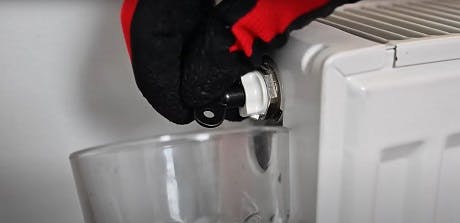 Main gantée dévissant la vis de purge d'un radiateur