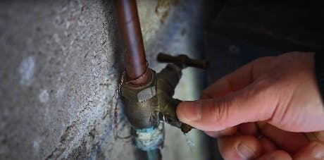 Main actionnant un robinet d'arrêt rouillé sur un mur en pierre