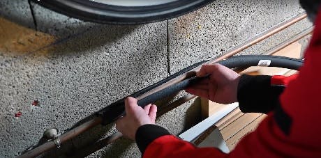 Mains en vêtement rouge travaillant sur un câble longeant un mur en béton