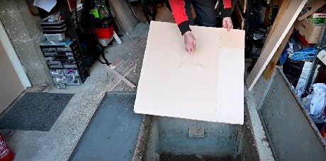 Main soulevant un panneau blanc au-dessus d'une trappe au sol