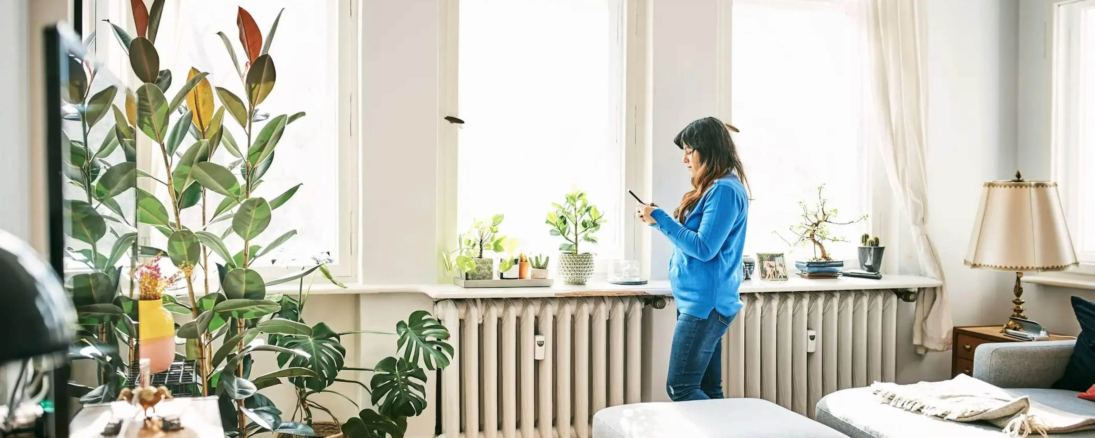 Femme consultant son téléphone devant un radiateur qui ne s'éteint plus dans un salon lumineux