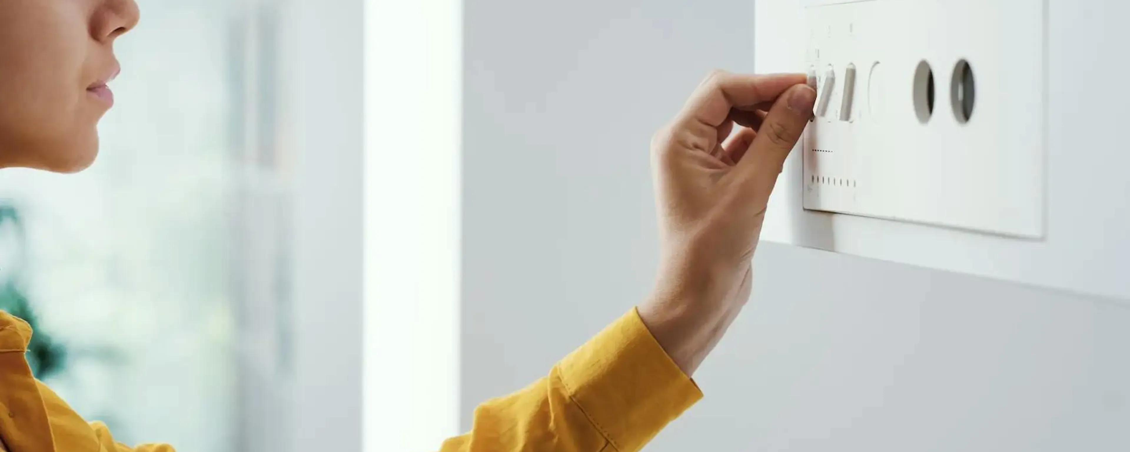 Femme réglant la température de sa chaudière murale à l'aide des curseurs du panneau de commande