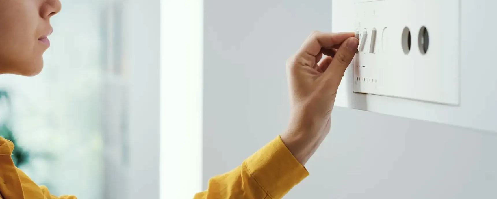 Femme réglant la température de sa chaudière murale à l'aide des curseurs du panneau de commande
