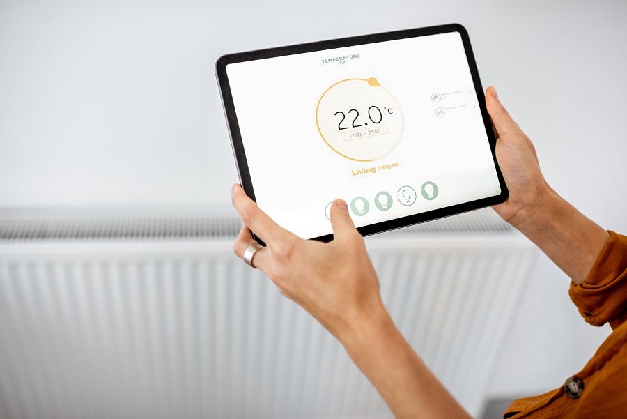 Mains tenant une tablette affichant un thermostat connecté à 22 degrés